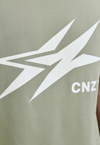 Camiseta de algodón verde olivo con un gran diseño gráfico blanco y el texto "CNZ" en blanco debajo. Textura suave y corte regular.