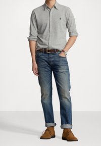 Grå långärmad skjorta, blå denimjeans med uppvikta fållar, bruna snörstövlar och ett brunt bälte. Klocka på handleden.