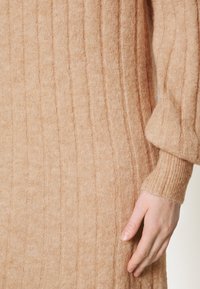 Abito a costine beige con maniche lunghe e finitura texturizzata. Il tessuto appare morbido e leggermente peloso, con polsini aderenti.
