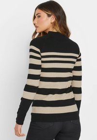 Gestreifter Pullover in Schwarz und Beige mit hohem Kragen, langen Ärmeln und Knopf-Details an den Seiten. Der Stoff hat eine glatte Textur.