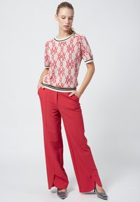 Top de punto rojo con estampado y mangas cortas, ribete negro, combinado con pantalones de pierna ancha rojos de cintura alta con aberturas. Zapatos con acentos plateados.