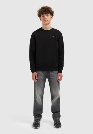Zwart sweatshirt met ronde hals, met een subtiele logo op de borst. Gecombineerd met lichtgrijze spijkerbroeken en zwart met patroon sneakers.