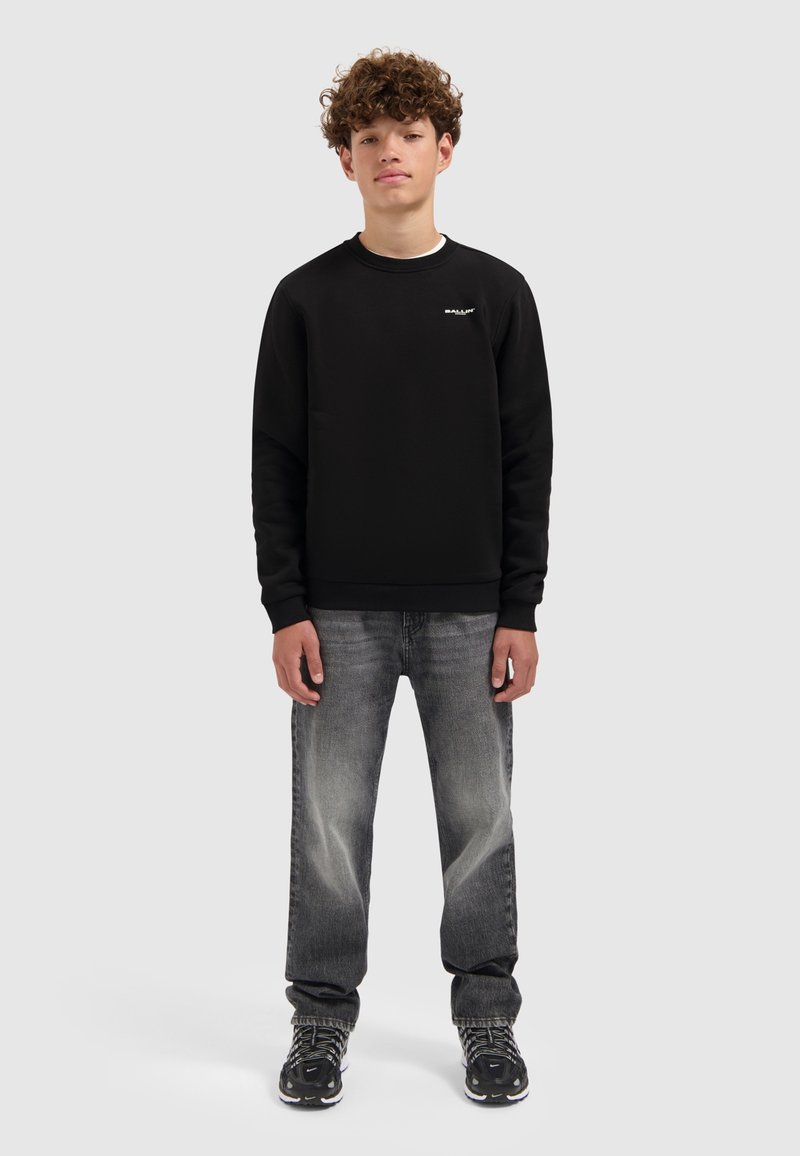 Zwart sweatshirt met ronde hals, met een subtiele logo op de borst. Gecombineerd met lichtgrijze spijkerbroeken en zwart met patroon sneakers.