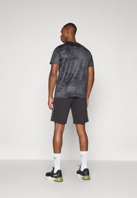 Camisa preta de manga curta com uma textura subtil, combinada com calções pretos com riscas laterais estampadas e ténis pretos e verdes.