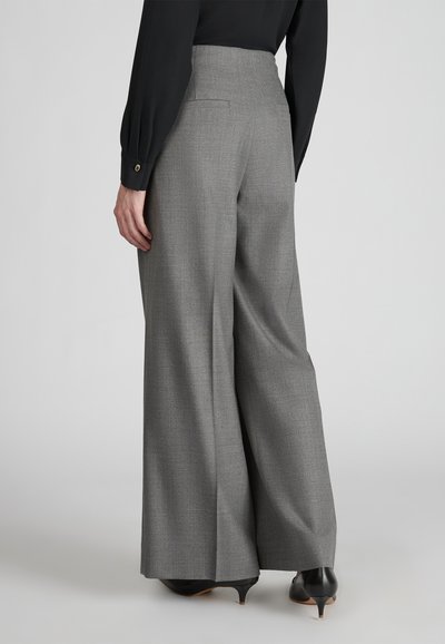 Szare spodnie typu wide-leg wykonane z lekkiego materiału; charakteryzują się gładką teksturą i detalem tylnej kieszeni. Połączone z czarnymi szpilkami.