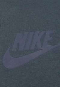 Mörkblått texturerat tyg med en stor, dämpad marinblå Nike-logotyp och swoosh, prägling för en subtil upphöjd effekt.