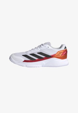 Zapatilla deportiva blanca con rayas negras, parte superior de malla texturizada, un detalle en el talón rojo y naranja, y suela de goma blanca.
