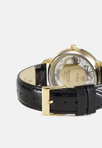 Orologio d'oro con fondo trasparente, cinturino in pelle nera lucida e fibbia dorata, con quadrante circolare e dettagli del quadrante ben evidenti.