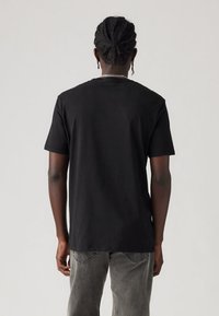 Juoda medvilninė marškinėliai su trumpomis rankovėmis ir apvalia iškirpte, pasižymintys laisvu modeliu ir lygiu paviršiumi. Nugaros pusėje nėra jokių grafinių elementų ar papuošimų.