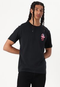 Sort t-shirt lavet af bomuld, med et pink grafisk design på brystet, korte ærmer og en afslappet pasform.