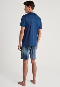 T-shirt a maniche corte blu navy abbinato a pantaloni a righe verdi, viola e blu. Il tessuto sembra leggero e liscio.
