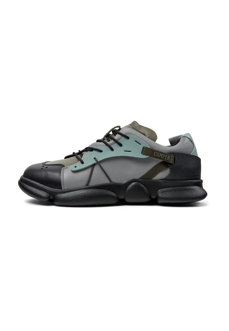 Sneaker caratterizzata da un mix di materiali neri, grigi e turchesi, con una forma arrotondata, suola texturizzata e un sistema di allacciatura prominente.