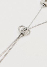 Sølvjusterbar slider med klare rhinsten på to tynde, fleksible sølvkæder mod en hvid baggrund.