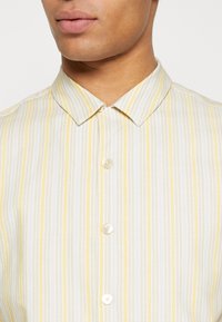 Camicia a maniche corte con colletto, caratterizzata da strisce verticali gialle e bianche e chiusura con bottoni su un tessuto leggero.