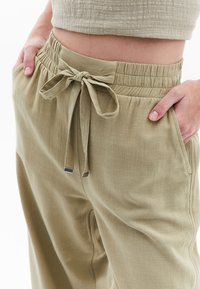 Licht olijfgroene broek met een elastische tailleband, strikdetail en zijzakken. Geweven stof met een losse, relaxte pasvorm.