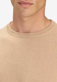 Beige neulepaita, jossa on pyöreä pääntie. Suunnittelu on yksinkertainen ja pinta on sileä. Kuvan lähikuva korostaa kankaan yksityiskohtia ja kauluksen tyyliä.