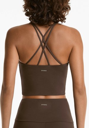 Brown sports crop top with crisscross straps, made of smooth fabric. Features a logo at the back and pairs with matching high-waisted bottoms.