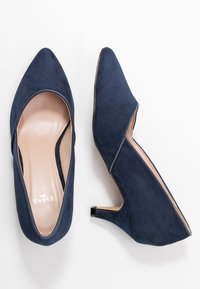 Chaussures à talons hauts en daim bleu marine avec bout pointu, design découpé et semelle intérieure beige contrastante. Elles présentent un petit talon épais.
