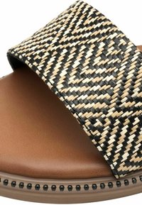 Sandal jalkapehmusteella, jossa on leveä musta ja beige kudottu hihna ja ruskea pehmustettu pohja, sekä mustia niittejä matalaosan varrella.