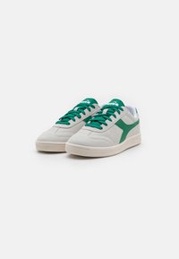 Lys grå semsket sneakers med grønne detaljer og snøringer, med polstret krage og teksturert gummisåle. Rund tådesign.