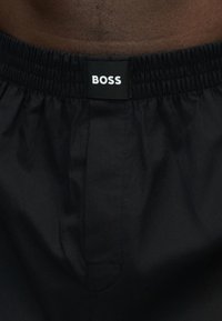 Gros plan sur un short noir à taille élastique avec une étiquette noire affichant "BOSS" en lettres blanches au centre devant.