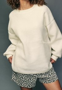 Biały, oversize'owy sweter z polaru z prążkowanymi mankietami, zestawiony z beżowymi i czarnymi szortami w panterkę. Miękka tekstura i luźny krój.