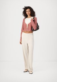 Cárdigan corto de cuadros vichy en rojo y blanco con nudo en la parte delantera, combinado con pantalones de lino beige de pierna ancha y zapatos planos de color claro. Bolsa negra.