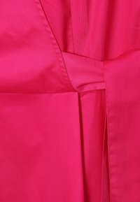 Tissu rose vif avec une texture lisse et un léger éclat, présentant un design plié avec des plis et des détails de couture soignés.