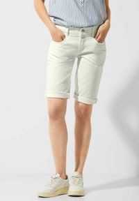 Jasne dżinsowe szorty z podwiniętymi mankietami, przednimi kieszeniami i płaskim przodem. Nosi się je z niebieską i białą koszulą w paski.