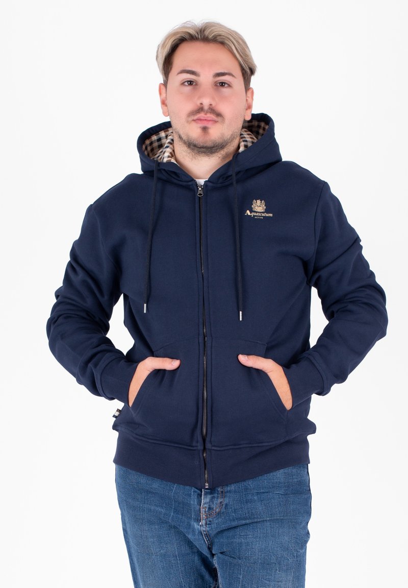 Felpa con zip blu navy, dotata di cappuccio, tasche frontali e fodera a quadretti. Presenta ricamo del logo sul petto e un tessuto testurizzato.