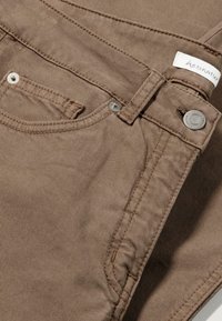 Bruine denim broek met een gestructureerde geweven textuur, een voorzak en metalen knoopaccenten, met een label aan de tailleband genaaid.