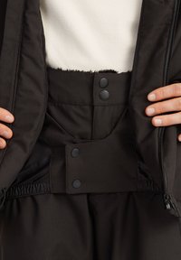 Čierna izolačná bunda so zipsom, vybavená patentkami a elastickým pásom. Interiér je podšitý mäkkým materiálom.