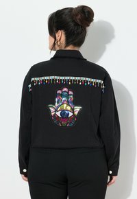 Musta takki, jossa on värikäs käsi- ja silmäkirjonta selässä, koristeltuna monivärisillä helmiaksentteilla olkapäillä.