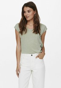Camiseta de manga corta verde claro con un brillo sutil, combinada con unos vaqueros blancos de tiro alto. Diseño sencillo, textura suave y ajuste cómodo.
