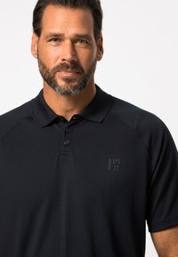 Polo noir avec col, en tissu texturé et doté de trois boutons. Un petit logo est visible sur la zone de la poitrine gauche.