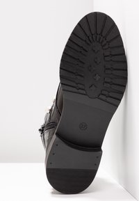 Semelle de chaussure noire avec motif de bande de roulement profond, taille 37 marquée, fermeture éclair latérale visible et décorations perlées sur le côté supérieur.