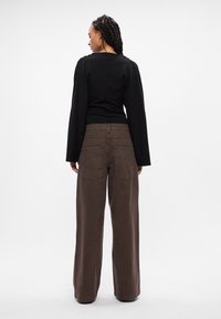 Top negro de corte relajado con mangas largas y escote redondo, combinado con pantalones de pierna ancha marrones de cintura alta que cuentan con bolsillos traseros.