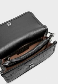 Bolso de mano de cuero negro con logotipo en relieve. Cuenta con un compartimento con cremallera y una textura suave. El interior es de tela marrón con un sutil brillo.