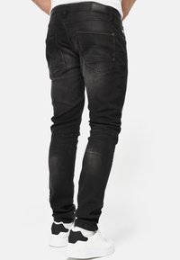Zwarte denim jeans met een slim fit, vijf-pocket ontwerp, lichte vervaging en contrasterende stiksels. Gecombineerd met witte sneakers.