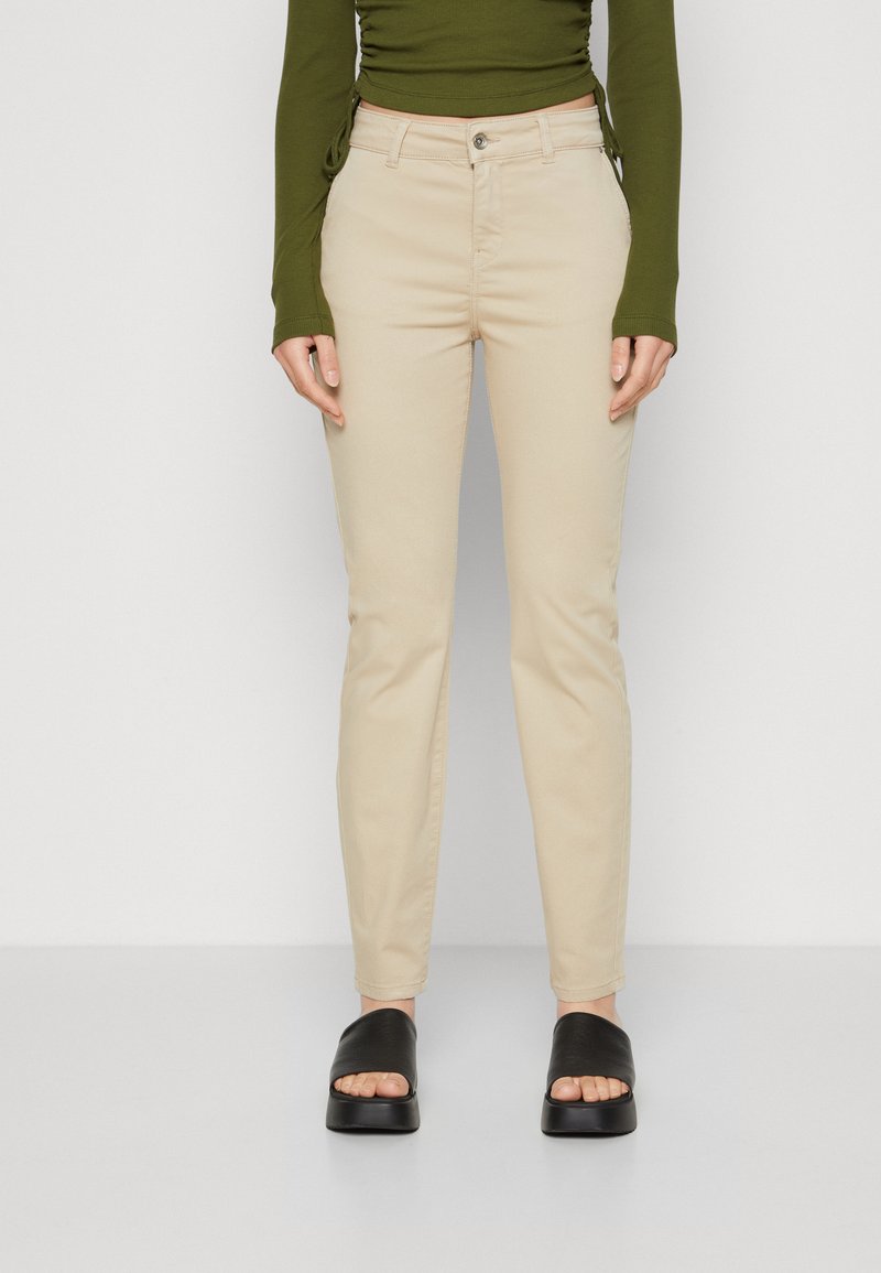 Beige slim-fit jeans med glidelås foran og frontlommer, laget av en glatt bomullsblanding. Kombinert med svarte sandaler med glid.