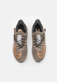 Sportschoenen met een beige gestructureerde bovenkant, oranje accenten, zwarte veters en een gevoerde zool. Stevig ontwerp, geschikt voor sportieve activiteiten.