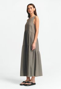 Rankų darbo olivinės spalvos suknelė be rankovių su pakeltu sijonu, pagaminta iš lengvos medžiagos. Derinkite su juodais plokščiais sandalais.