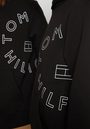 Sorte hættetrøjer med hvidt omrids af teksten "Tom Hilfiger" arrangeret i et cirkulært mønster og et rektangulært logo på fronten.