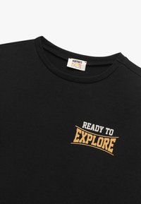 Czarna bawełniana koszulka z okrągłym dekoltem, z napisem "READY TO EXPLORE" w żółtym i białym kolorze oraz miękką teksturą. Z metką Koton Kids.
