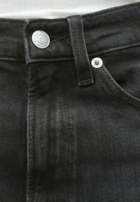 Μαύρο τζιν από τζιν ύφασμα με ίσια γραμμή, ασημένες λεπτομέρειες και αντίθετη ραφή στη μέση και τις τσέπες.