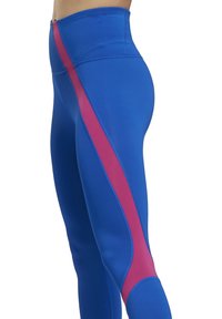 Detail osoby v modrých sportovních legínách se svislým růžovým pruhem podél vnější strany nohy.