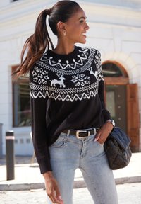 Schwarzer gestrickter Pullover mit weißem Fair-Isle-Muster, das Rentiere und Schneeflocken zeigt, kombiniert mit hellblauen Jeans und einer schwarzen gesteppte Handtasche.