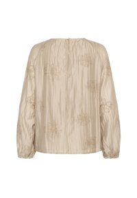 Blouse beige ample avec une finition texturée et brillante, ornée de broderies florales et de poignets élastiqués. Fermeture éclair au dos visible.
