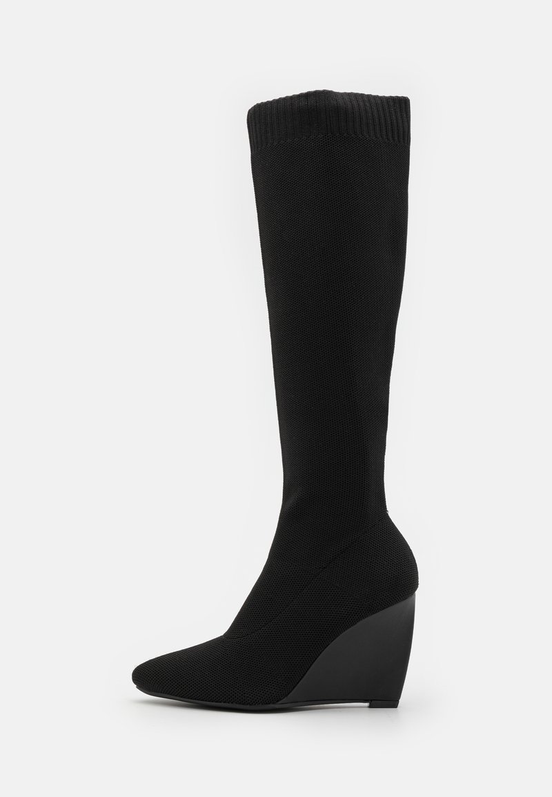 Bottes noires jusqu'au genou avec un dessus en tissu texturé, un bout pointu et un talon compensé. Couleur unie avec un détail de poignet côtelé.