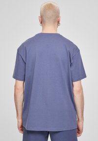 Tricou oversized din bumbac, de culoare purpurie, cu mâneci scurte, decolteu rotund și un design simplu. Textură netedă, fără modele sau accente vizibile.